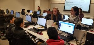 Fordham students address high school students seated at computers.