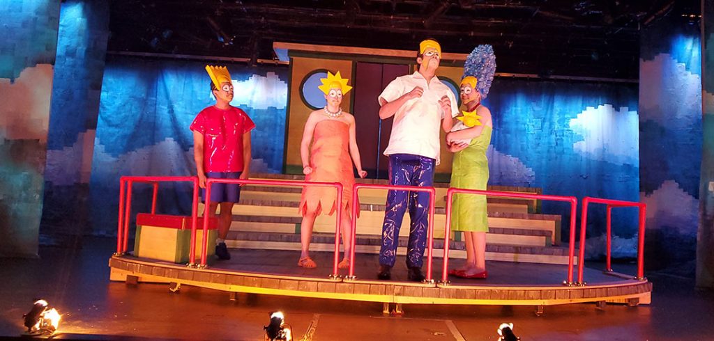 The cast of Mr. Burns dressed as Bart, Lisa, Homer and Marge, on stage in Pope Auditorium.