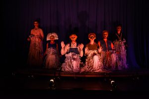 A group dressed like a Greek chorus kneels on stage at pope Auditorium