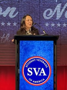 A woman wearing glasses speaks at a podium.