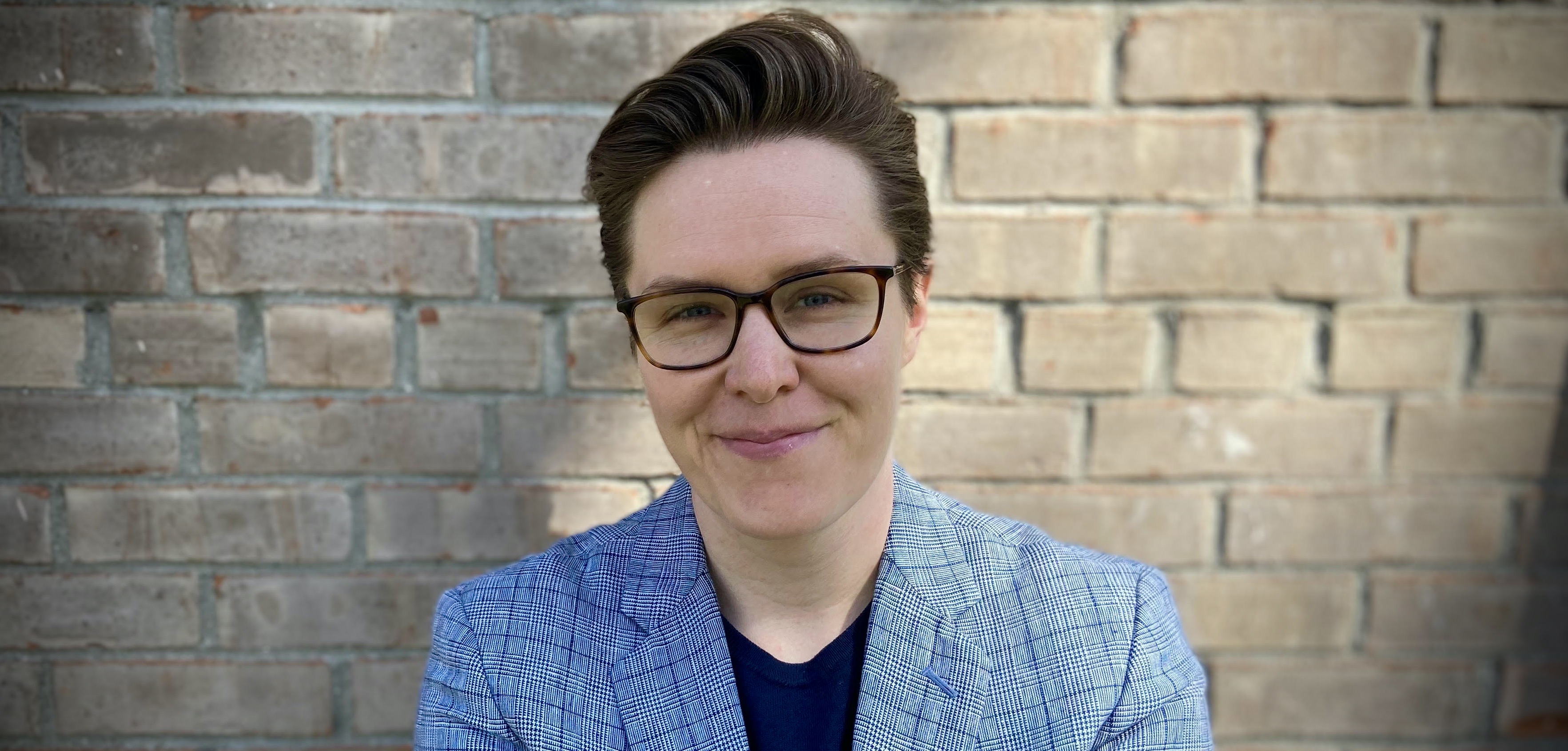 A woman wearing glasses and a blazer smiles.