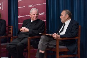 Monsignor Shelley sits on stage next to Joseph Joseph Cammarosano