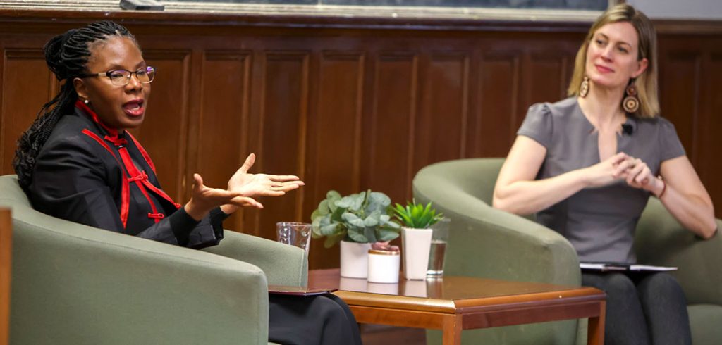 Melanie Harris seated on stage next to a table, with Christiana Zenner seated on the other side.