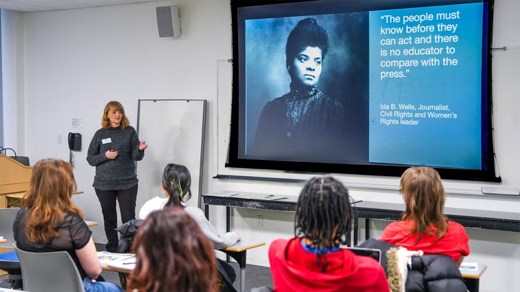 A woman stands in front of a classroom of students.