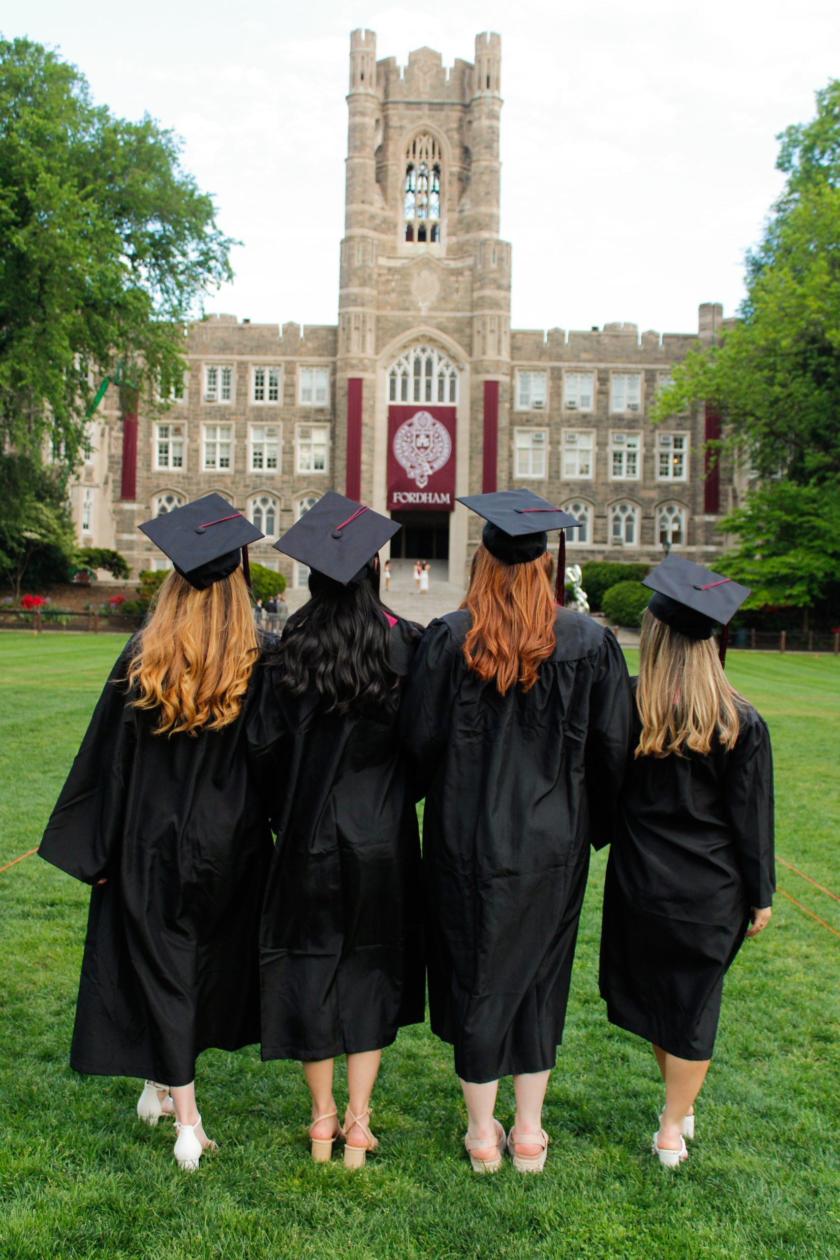 4 women facing away, in caps and gowns on Eddies parade. Looking at Keating Hall.
