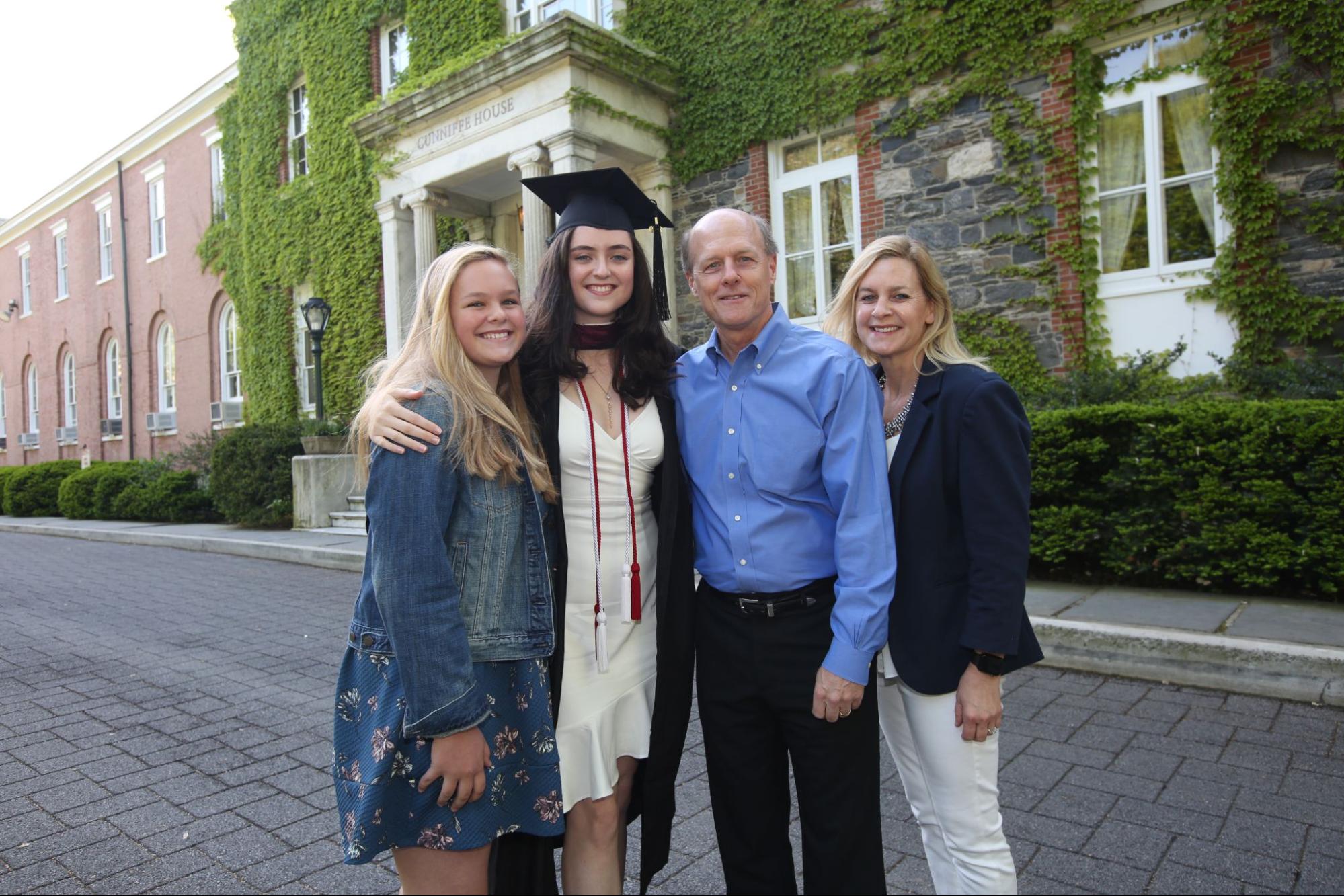 Female graduate in cap and gown with her family in front of ivy covered building