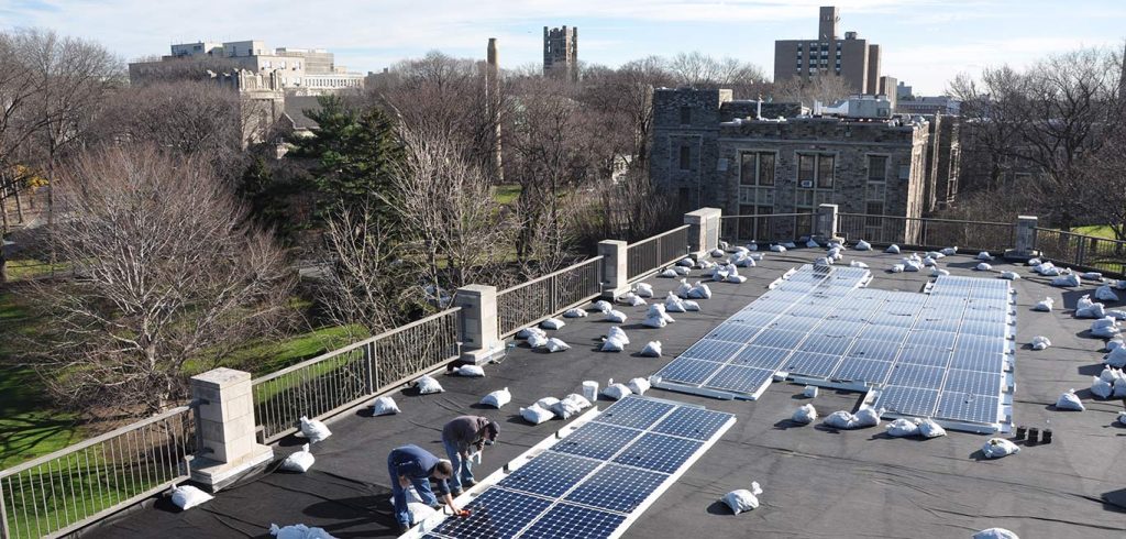 Workers install solar panels on the roof of a building on Fordham's campus.