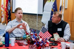 Two men sit at a table at Butler Commons festooned with an American flag.