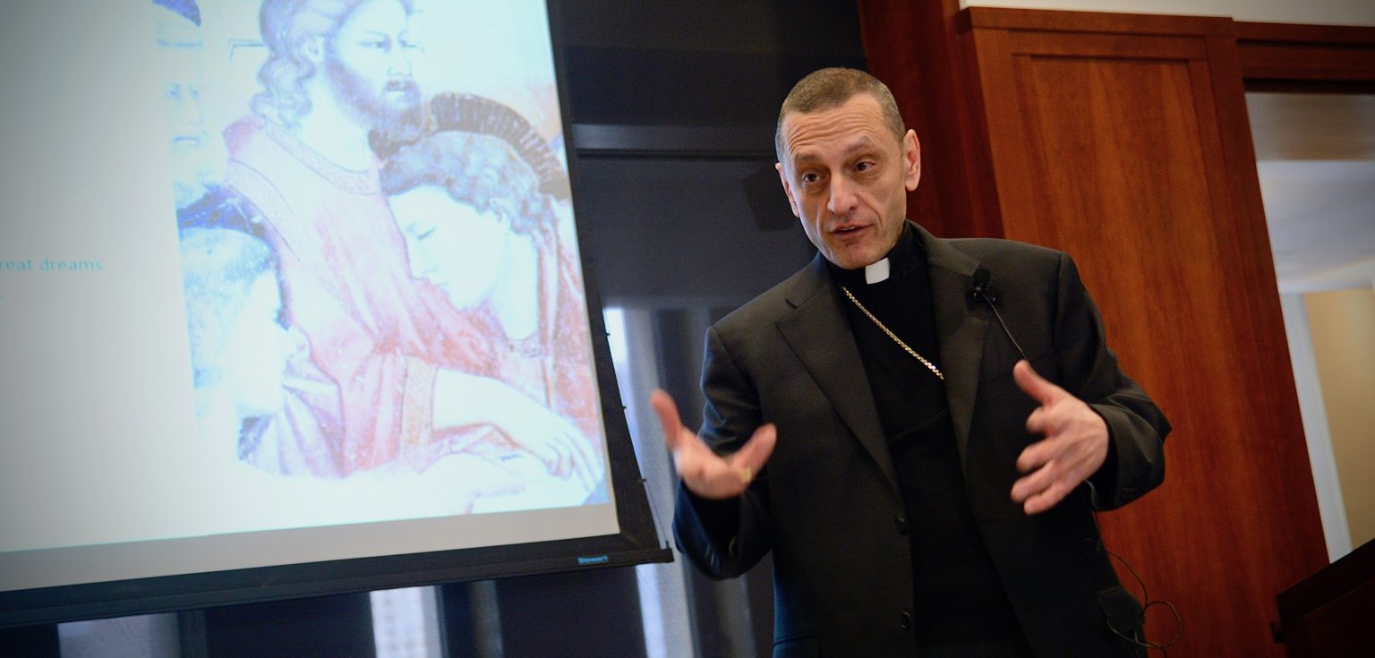 Bishop Caggiano gestures with his hands in front of a PowerPoint slide.