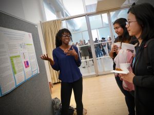 Itunu Ademoyo gestures toward her poster as students look on.