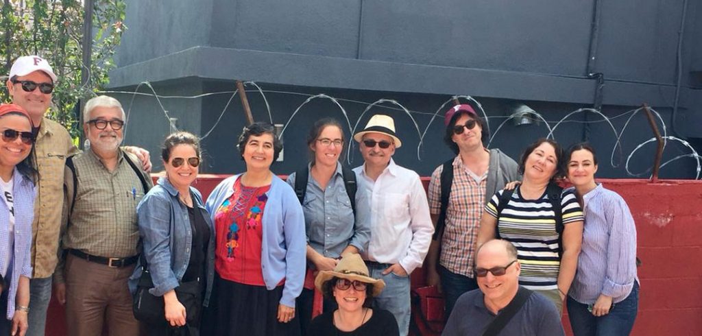 Fordham faculty members pose for a picture in front of a red wall topped with razor wire