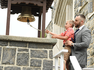 Graduating student veteran Wesley Wilson helps his 9-year-old nephew ring the Victory Bell