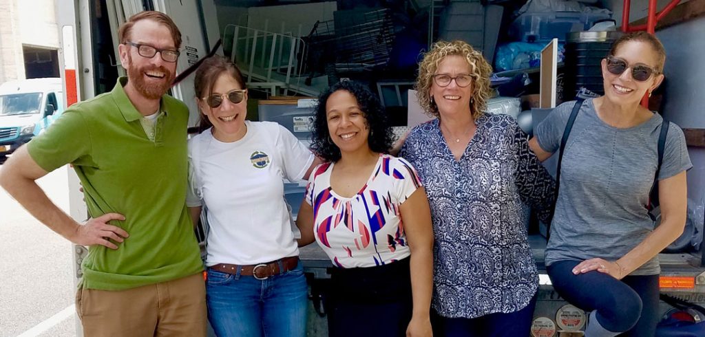 Five people smiling in front of a truck loaded with used dormitory items