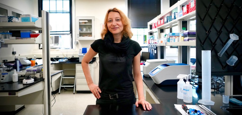 A woman wearing a black outfit stands in the center of a lab.