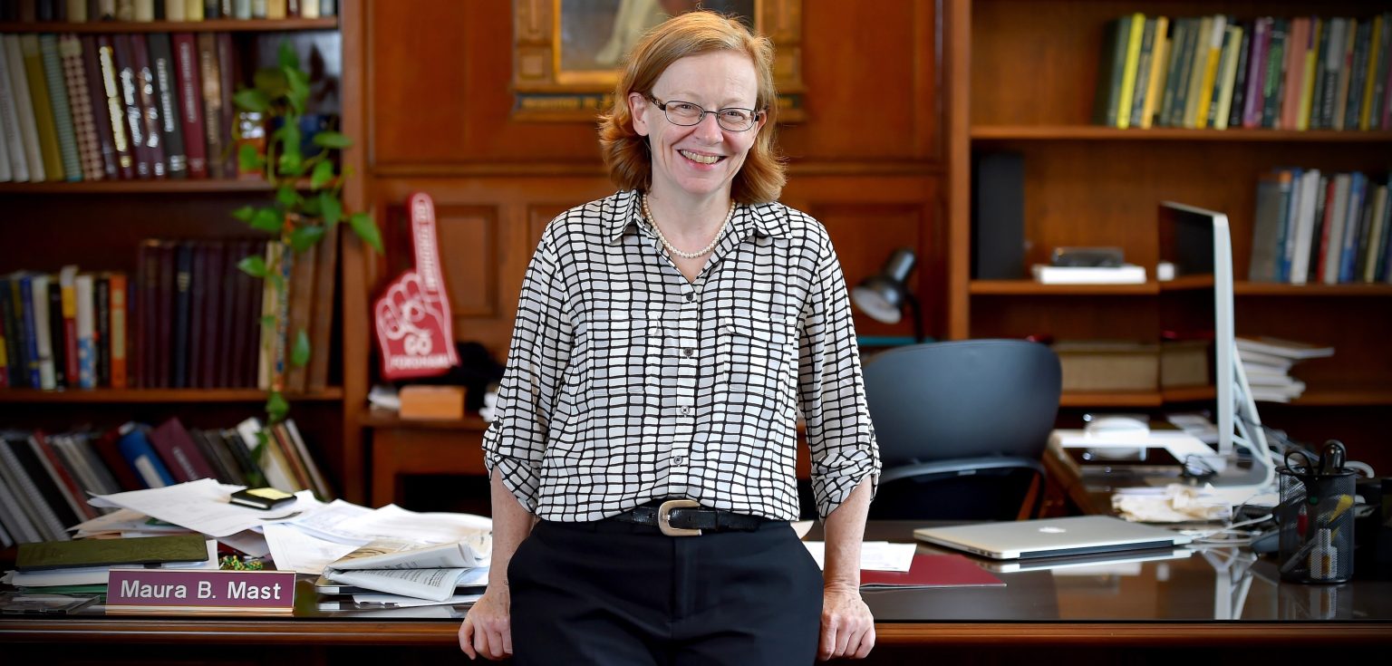 A woman stands in an office with her hands propped against a desk.