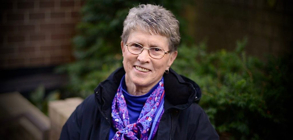 A woman wearing a jacket and purple floral scarf smiles.