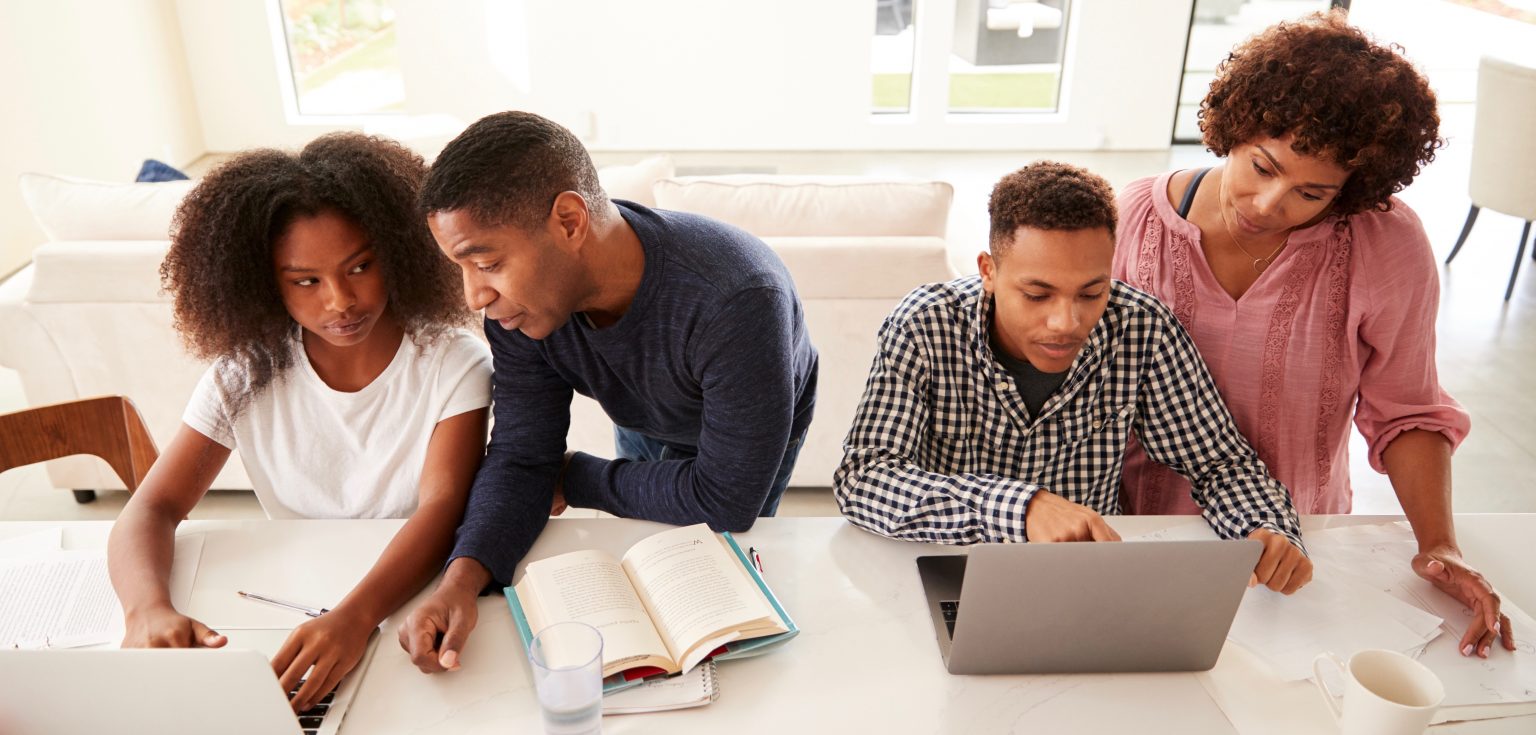 A girl, man, boy, and woman work in front of laptops and books.