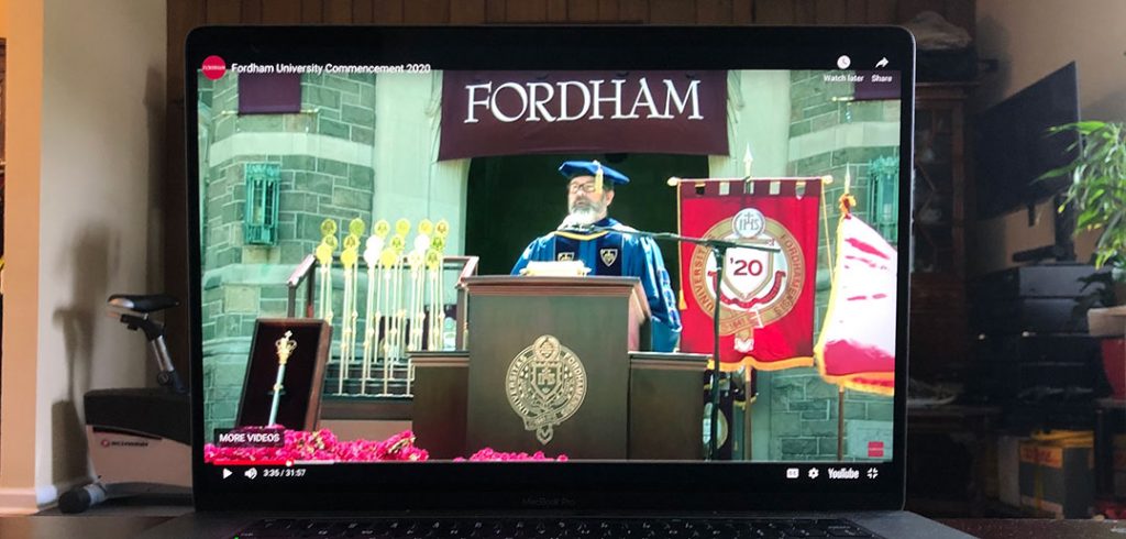 Father Mick McCarthy speaks at podium, while viewers watch on their computers.