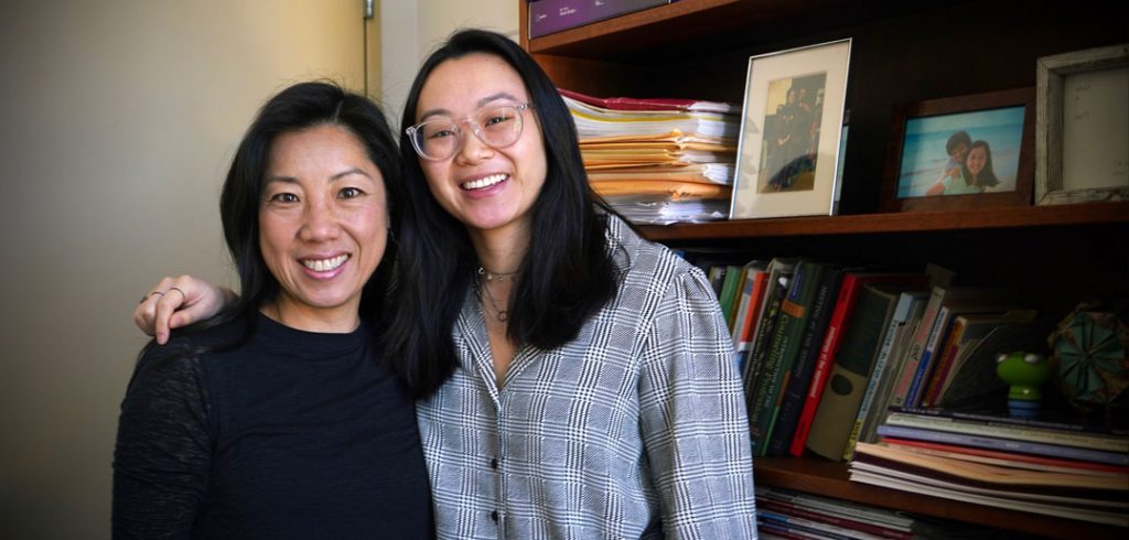 Two women stand and smile in front of a bookshelf.