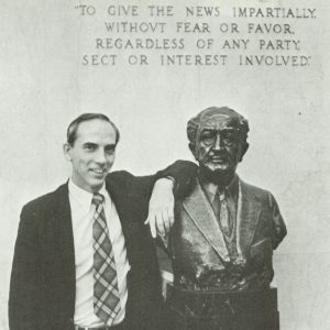 A black and white photo of a man standing beside a bust