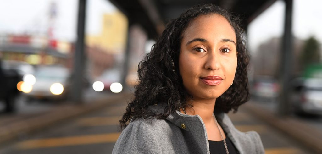 A portrait of author Naima Coster, a Fordham graduate, underneath an elevated train track in Brooklyn