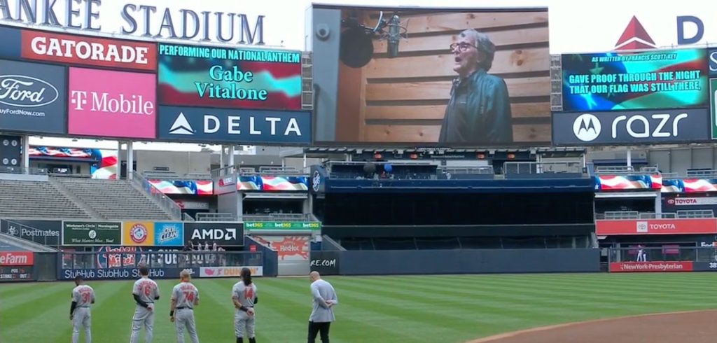 Baseball players stand on the field as the national anthem is sung.