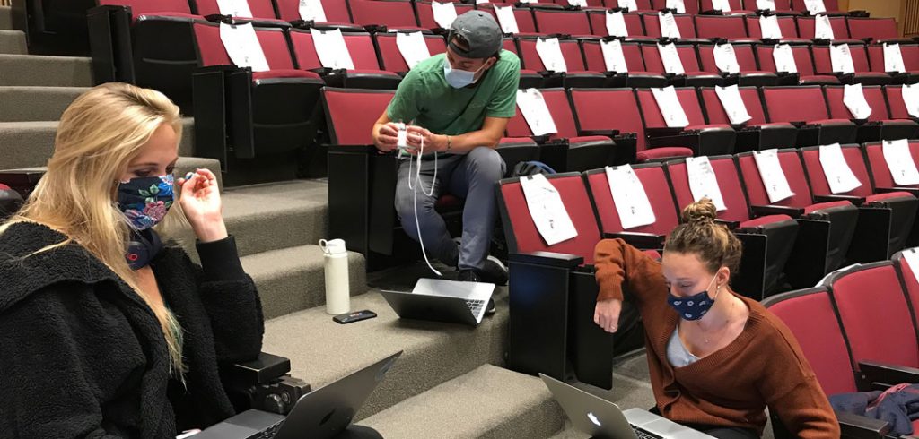 Three students sit spaced out in an auditorium