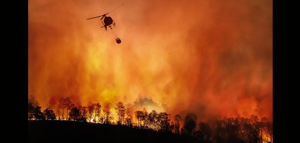 A helicopter flying above a burning landscape