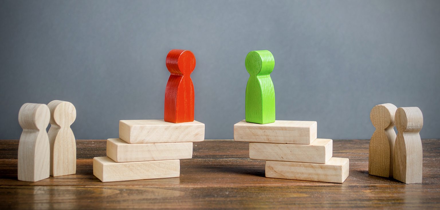 A red block figurine and a green block figurine on top of a pile of wooden blocks