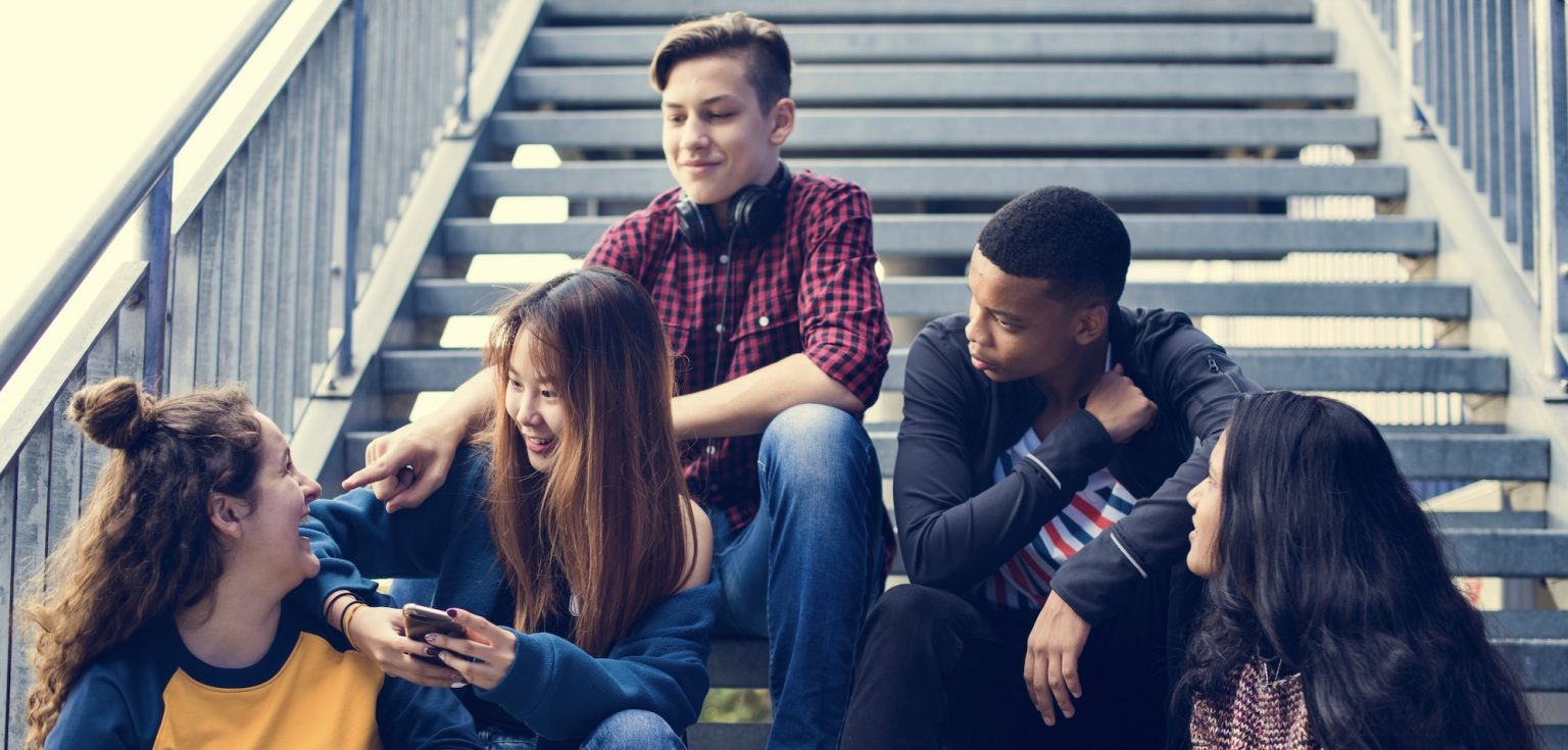 Five teenagers sit on a stairwell and chat.