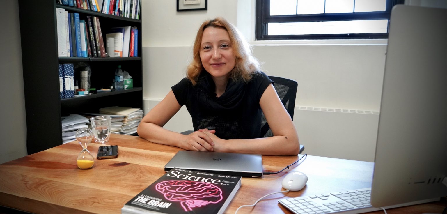 A woman smiles in front of a desk.