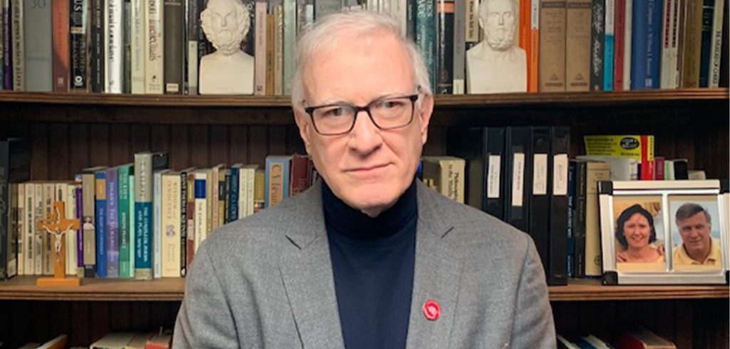 Tom Hughes, GSAS ’79, poses in front of a bookshelf.