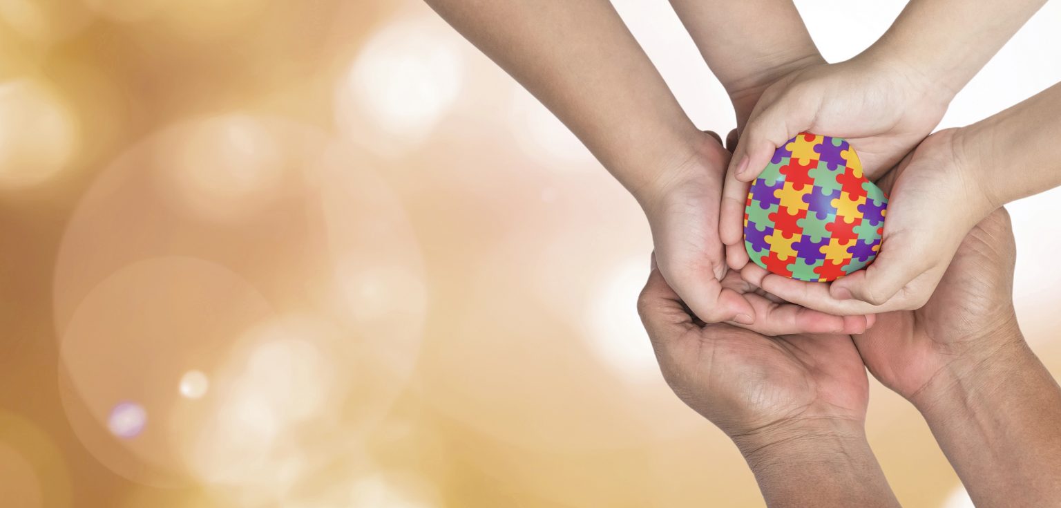 Three pairs of outstretched hands clasping a heart with a jigsaw puzzle design