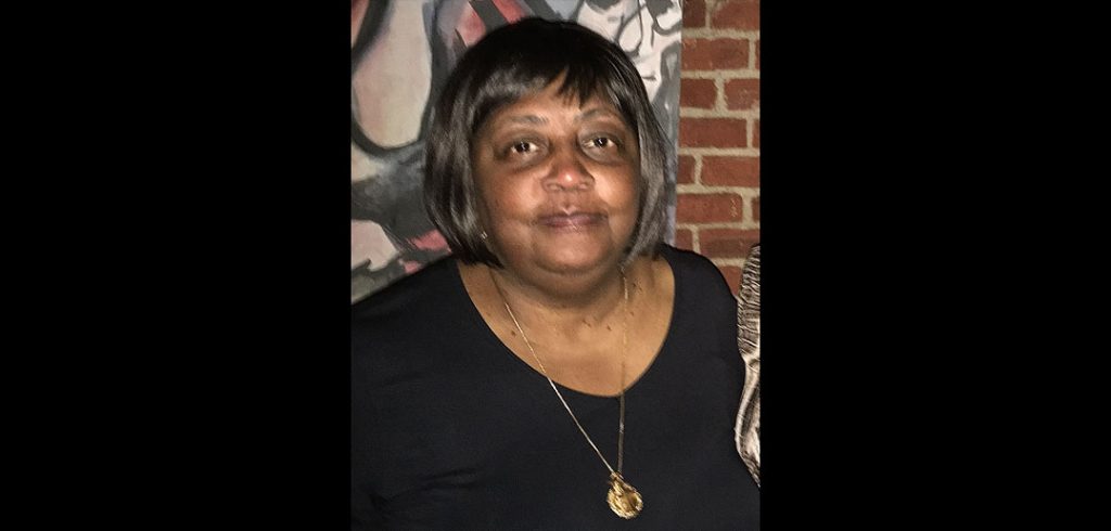 A woman wearing a black shirt and necklace smiles at the camera.