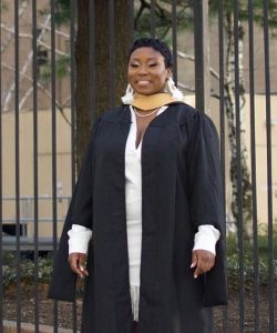 grad in front of iron gate in cap and gown