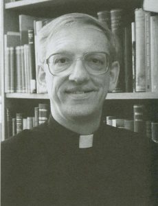 A man wearing glasses and a black Jesuit outfit smiles at the camera.