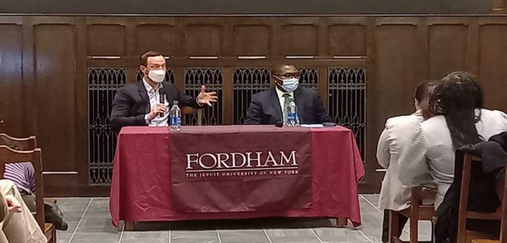 two men in masks at table giving lecture