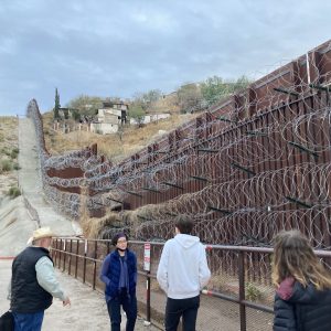 Four people stand in front of a wall that is twice their size in an outdoor setting.