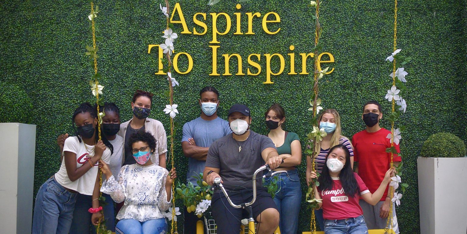 A group of masked students pose under a sign that says "Aspire To Inspire."