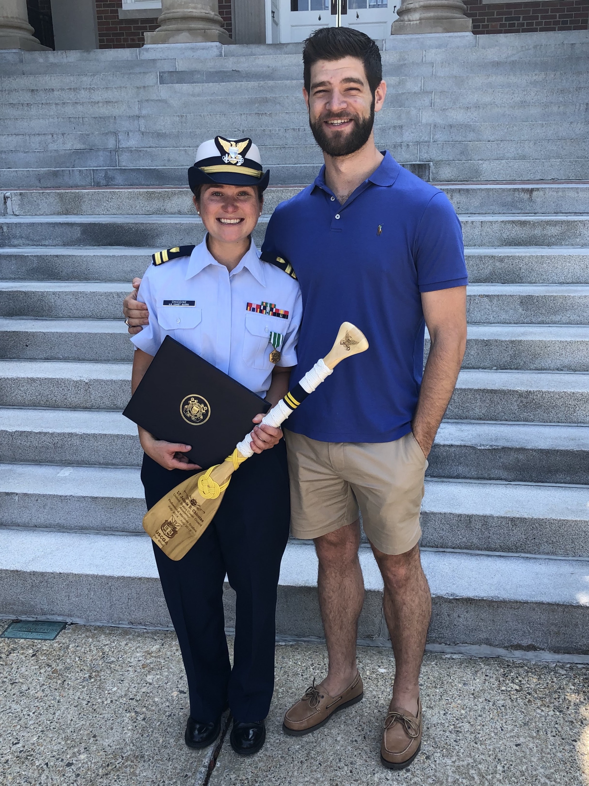 A woman wearing a Coast Guard uniform smiles next to a man wearing a blue shirt and cargo shorts.