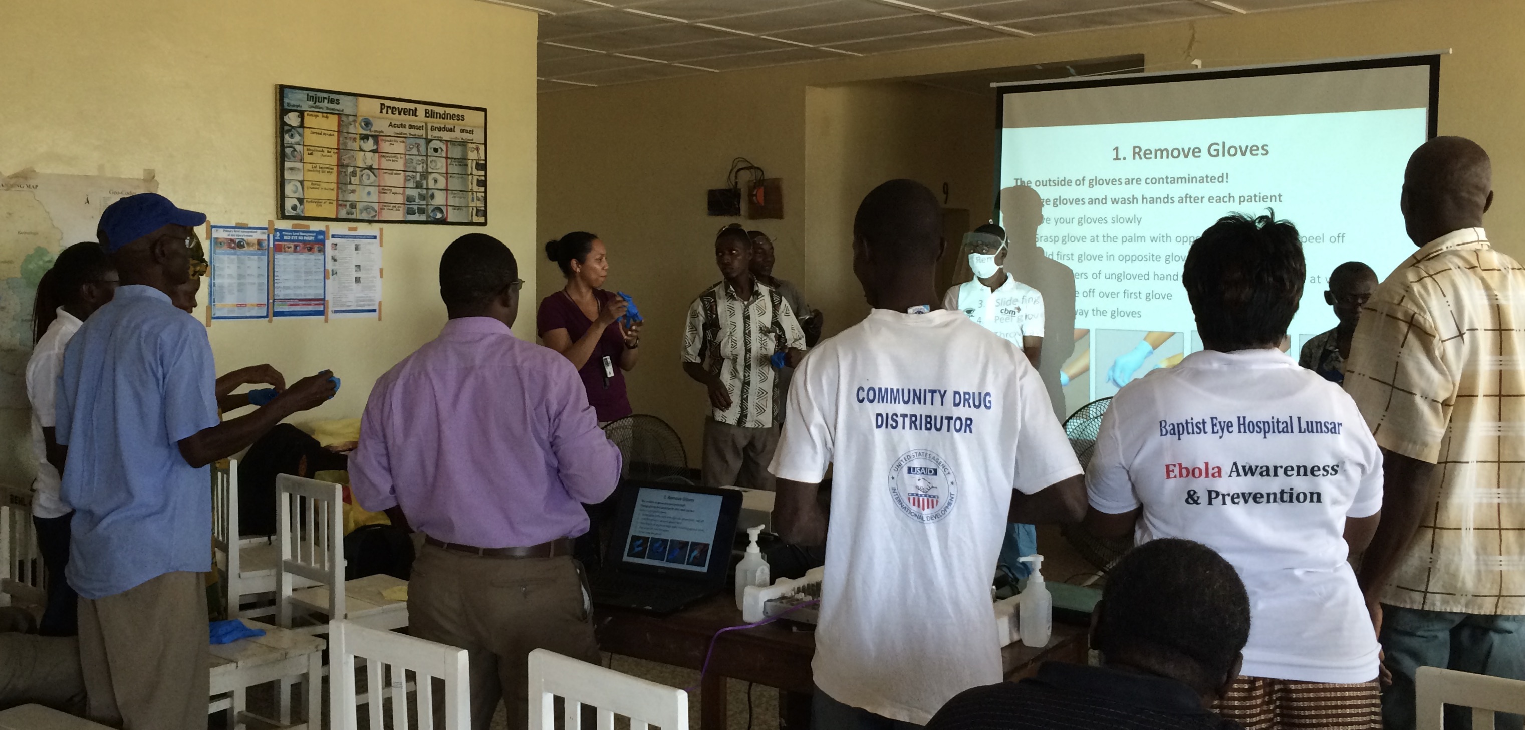 A woman speaks to a large group of people in front of a PowerPoint screen.