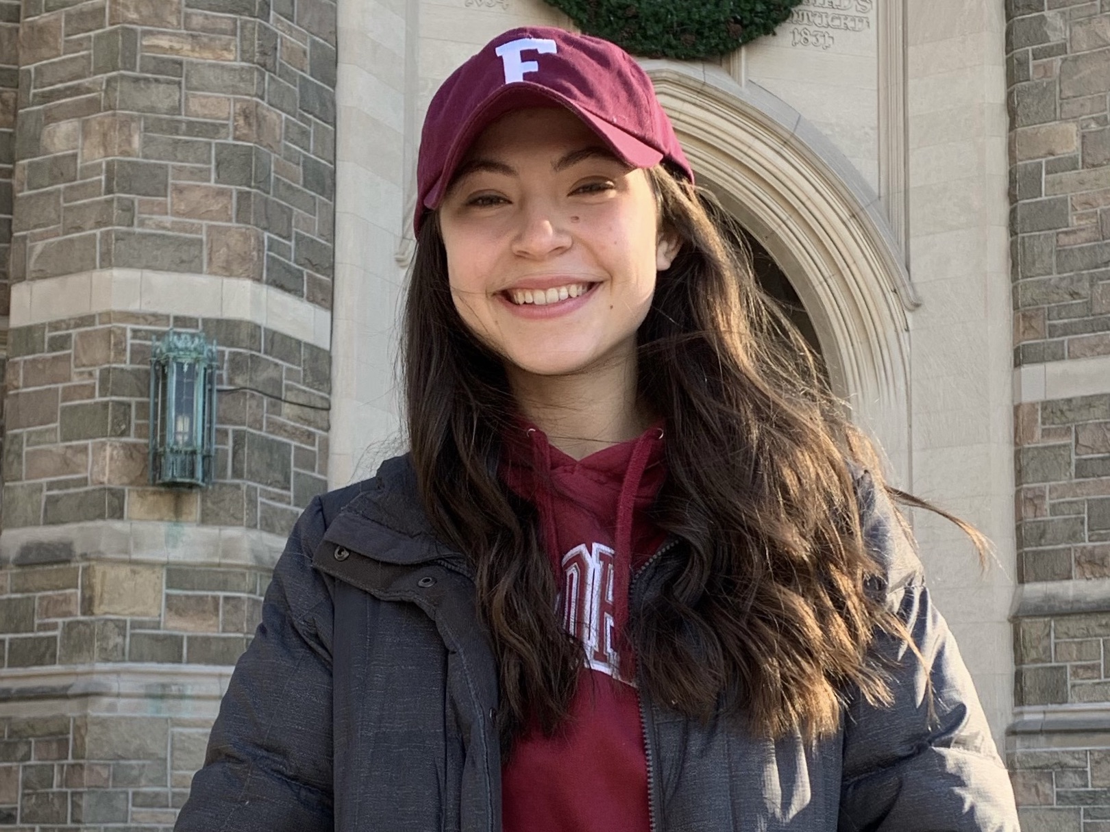 A brunette girl wearing a maroon baseball cap smiles.