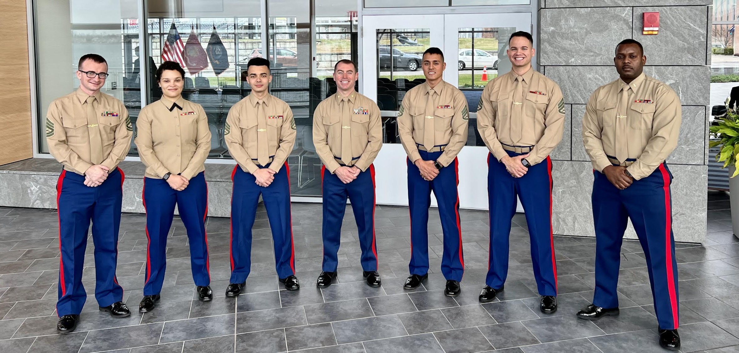 Seven people in uniform stand, hold their hands in front of each other, and smile.