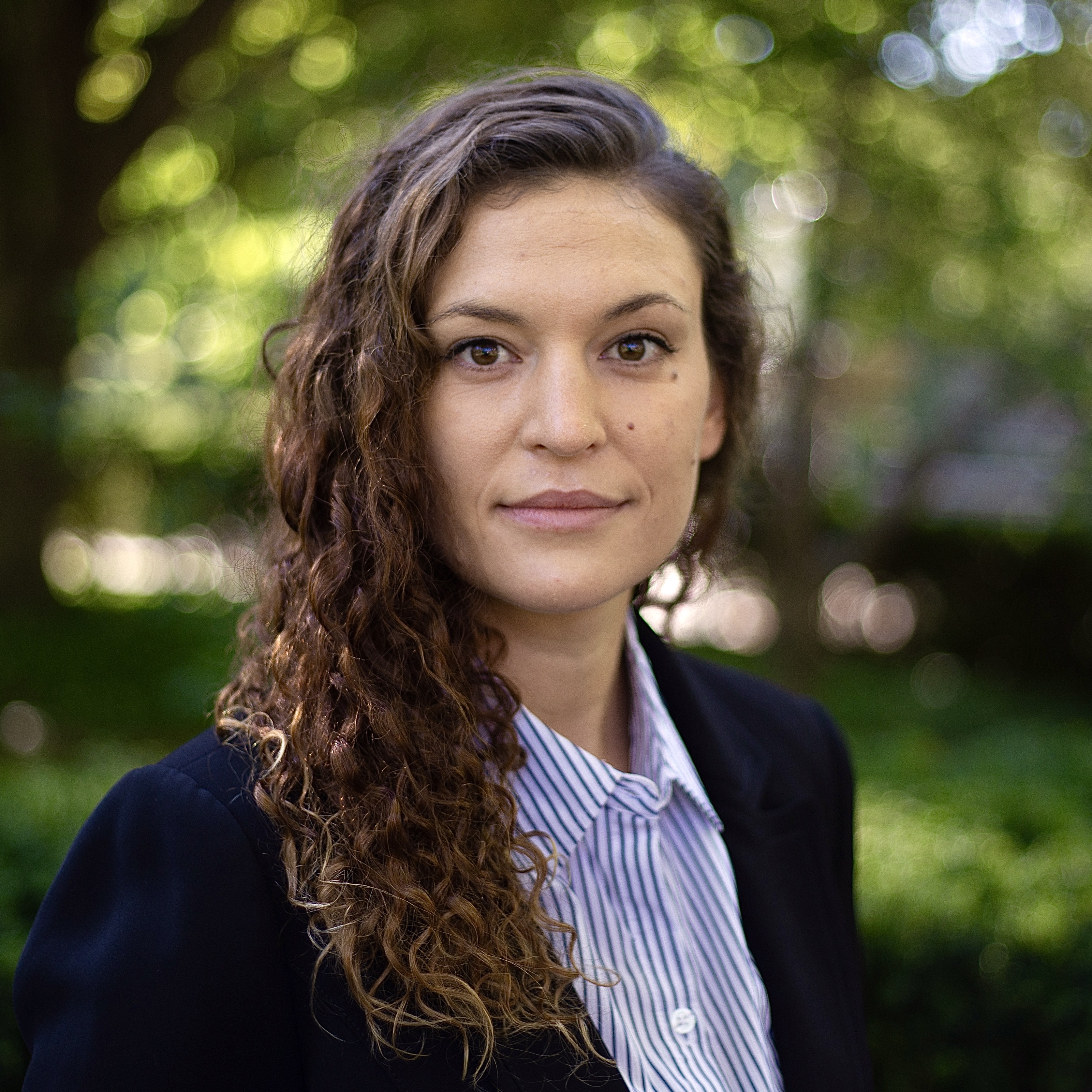 A woman with curly hair smiles with her mouth closed.