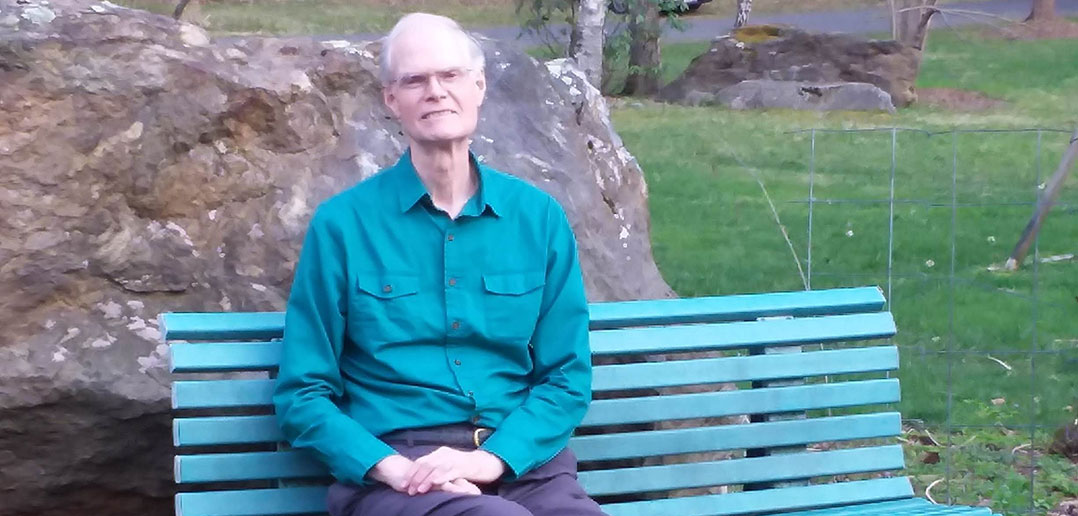 1965 Fordham graduate John Connolly sits on a bench in his backyard garden