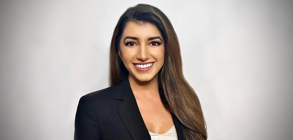 A woman wearing a blazer smiles in front of a blank background.