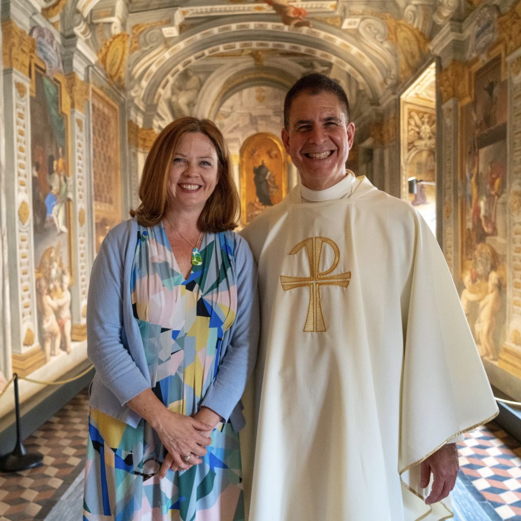 A woman and a man wearing a priestly white gown smile.