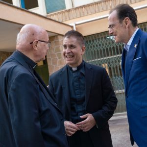 Three men wearing suits talk outside a building.