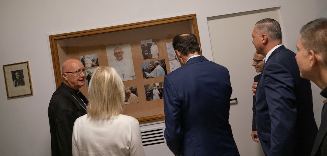 Several people observe a bulletin board filled with pictures.