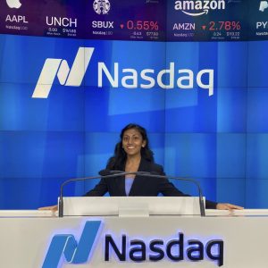 A woman wearing a business suit smiles in front of a white podium.